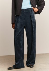 Marineblauwe corduroy wijde broek met voorplooien, gestructureerde stof en een zachte afwerking, gecombineerd met een lichtblauwe top en zwarte flats.