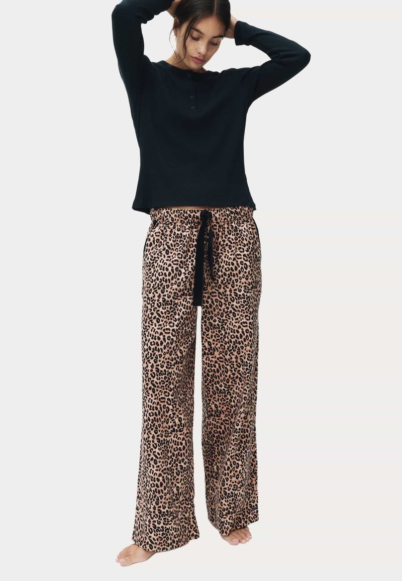 Sort ribbet langærmet top parret med beige leopardmønstrede sweatpants med snøre, der har en afslappet pasform og letvægtsstof. Ingen synlig hardware.