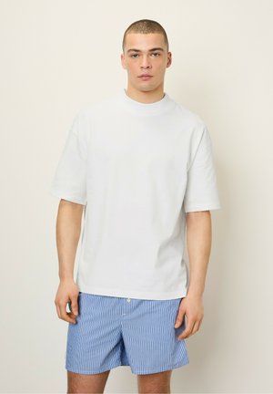 T-shirt en coton blanc à manches courtes et à col haut, assortie à un short bleu et blanc à rayures avec une fermeture à bouton à l'avant.