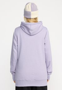 Sweat à capuche lilas avec une capuche à l'arrière, des poignets et un ourlet côtelés. Associé à un bonnet en tricot beige et violet. Matière en mélange de coton doux.