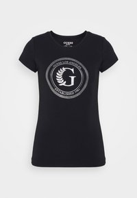 Sort bomulds T-shirt med korte ærmer, der har et cirkulært sølvlogo design og teksten "GUESS LOS ANGELES ETABLERET 1981."