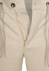 Beige geruite broek met een ritsluiting en verstelbare koordjes. Heeft een gladde textuur en een ronde, decoratieve knop.