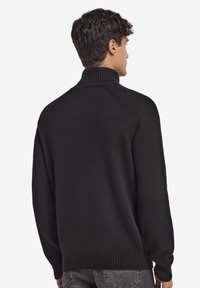Czarny dziany sweter z wysokim kołnierzem, ściągaczami na mankietach i na dole. Charakteryzuje się luźnym krojem i gładką teksturą. Bez wzorów i zdobień.