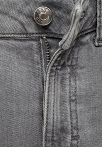 Sivi farbani denim materijal ima patentni zatvarač i metalnu dugmad sa ugraviranim tekstom "DENIM LAB". Detalji šivanja duž šavova su vidljivi.