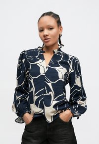 Bluza în model abstract bleumarin și crem, cu decolteu în V, mâneci bufante adunate și nasturi în față. Tesătură texturată cu o ușoară strălucire.