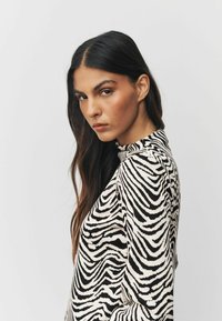 Čierno-biely prúžkovaný sveter s vysokým golierom a rebrovanou textúrou. Má dlhé rukávy a priliehavý strih, na bielom pozadí.