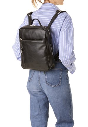 Zaino in pelle nera dal design elegante, con tasca frontale con zip e spallacci regolabili, indossato sulla schiena, abbinato a una camicia a righe.