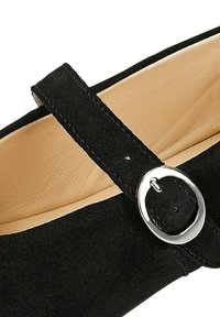 Černá semišová bota se strapcem, který zdobí stříbrná spona. Interiér je v tónech tan, což podtrhuje kontrast s vnějším materiálem.