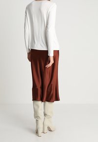 Vit långärmad topp i kombination med en brun satinkjol, kompletterad med knähöga beige stövlar med klack.