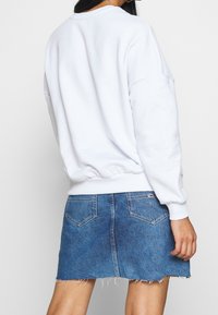 Felpa bianca con orlo e polsini a coste abbinata a una gonna di jeans con orlo sfrangiato. L'outfit presenta una silhouette casual e rilassata.