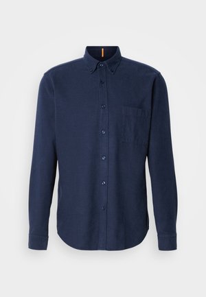 Jūras zila garām piedurknēm pogājama krekls, izgatavots no teksturēta auduma, ar krūšu kabatu un noapaļotu apakšmalu. Divu pogu apkakles detalizācija.