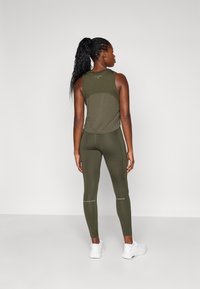 Olivgrünes sportliches Tanktop mit taillierter Passform und Rückeneinsatz. Kombiniert mit passenden Leggings mit Akzentdetails. Weiße Sportschuhe.