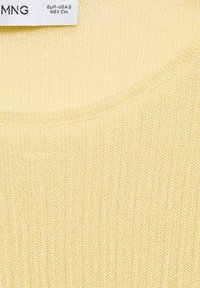 Rumena pletena jopica z okroglo izrezom. Tekstura ima fino navpično rebrasti vzorec, kar omogoča lahko in zračno kakovost.