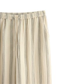 Beige randiga byxor med elastisk midja och dragsko, med vertikala linjer och en texturerad tyg. Inkluderar sidofickor.
