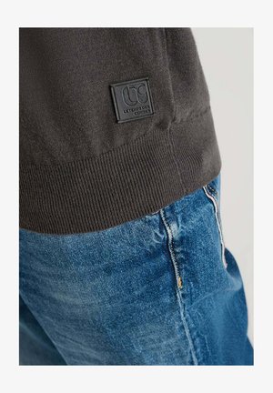 Donkergrijs gebreid sweater met geribbelde zoom en een zwart logo badge; gecombineerd met lichtblauwe denim jeans met contrasterende stiksels.