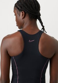 Čierny športový top s pretekárskym strihom, s ružovými švami a malým ružovým logom Nike na zadnej strane.