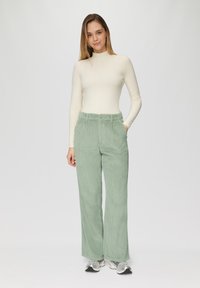 Lichtgroene corduroy wijde broek met een gestructureerd oppervlak, voorzien van een knoopsluiting en zijzakken, gecombineerd met een crèmekleurige geribde coltrui.