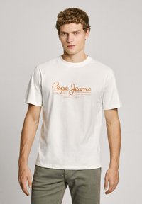 Biela bavlnená tričko s potlačeným logom "Pepe Jeans" v oranžovej farbe. Dizajn obsahuje aj ďalší text v menšom písme pod logom.