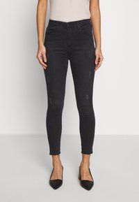 Jeans de denim negro ajustados con una cintura alta, detalles sutiles de desgaste y un diseño ajustado, acompañados de tacones negros de punta.}}