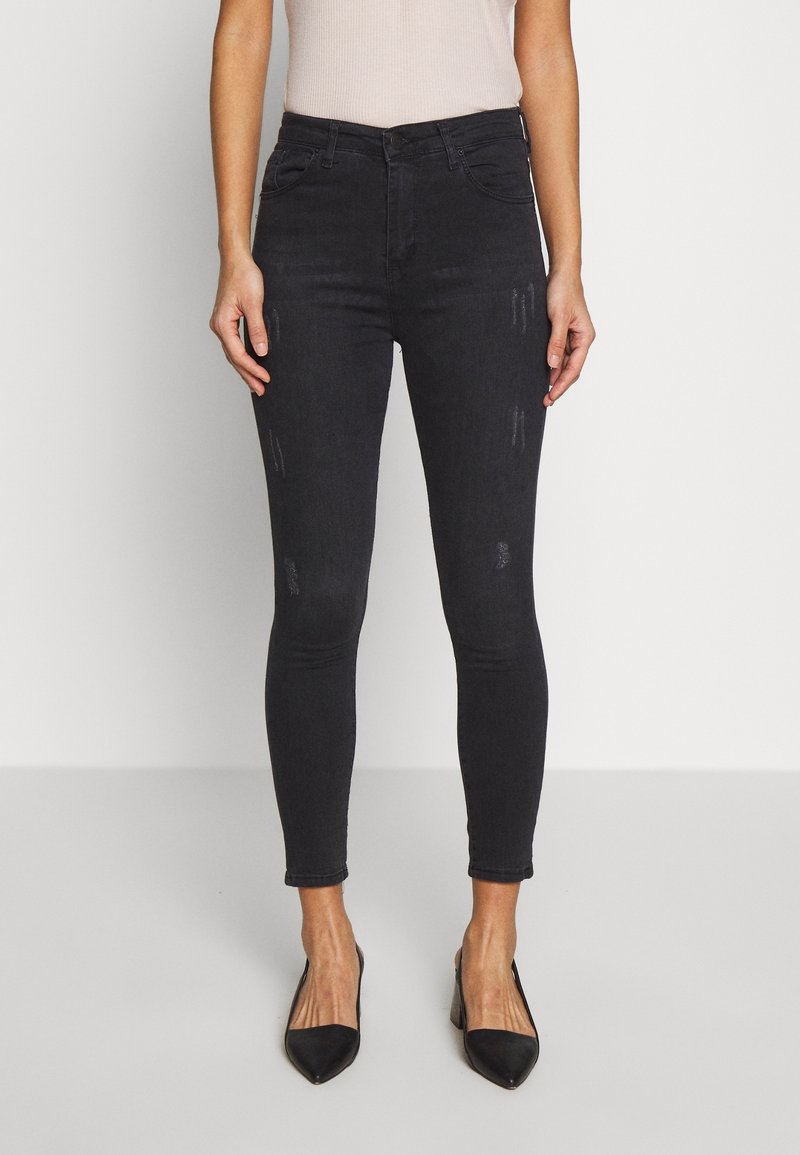 Jeans de denim negro ajustados con una cintura alta, detalles sutiles de desgaste y un diseño ajustado, acompañados de tacones negros de punta.}}