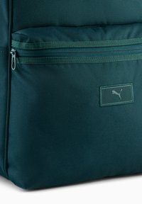 Ciemnozielony plecak z teksturowanej tkaniny, z przednią kieszenią na zamek oraz logo Puma na prostokątnej naszywce.