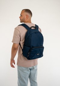 Navy blue backpack with a smooth texture, a front zipper pocket, and padded shoulder straps. Suitable for casual use, minimalistic design.