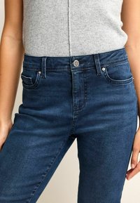 Dark blue high-waisted jeans feature a smooth denim texture, two front pockets, and a silver button closure at the waist.