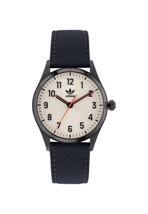 Montre noire avec un cadran beige, bracelet en textile bleu marine, chiffres arabes et aiguille des secondes rouge. Logo Adidas affiché sur le cadran.
