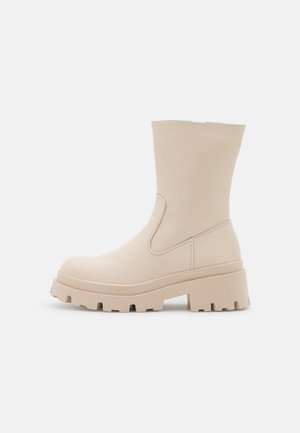 Botte mi-mollet couleur crème avec semelle épaisse crantée et talon carré, dessus en cuir lisse et détail de couture minimaliste.
