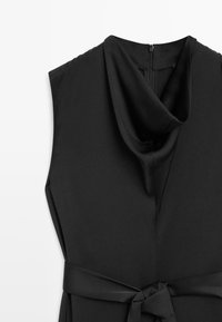 Zwart mouwloos jurkje met een gedrapeerde colhals, zijrits en een bijpassende stoffen riem die om de taille is gestrikt. Gladde textuur.