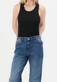 Top negro de canalé combinado con jeans de mezclilla azul de talle alto. Los jeans tienen un lavado desgastado y un diseño clásico de cinco bolsillos.