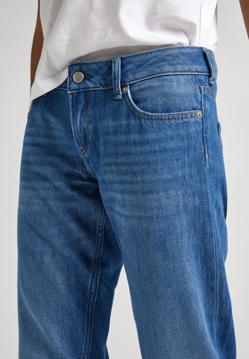 Blaue Denim-Jeans mit geradem Schnitt, Fünf-Taschen-Design und Metallbeschlägen mit einer dezenten, ausgewaschenen Textur. Gürtelschlaufen und nähtliche Details sichtbar.