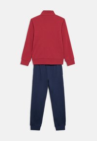 Κόκκινο φούτερ με γιακά και μπλε παντελόνι. Και τα δύο από μαλακό ύφασμα, με ελαστικά μανίκια και μέση, προσφέροντας άνεση και ευελιξία.