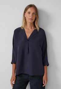 Blouse marine à col en V, manches trois-quarts et détail de pli à l'avant. Fabriquée en tissu léger.