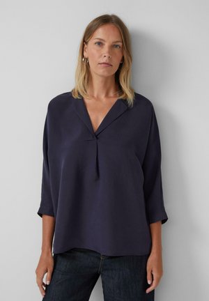 Blouse marine à col en V, manches trois-quarts et détail de pli à l'avant. Fabriquée en tissu léger.