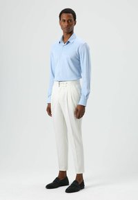 Light blue long-sleeve shirt with buttons, paired with white tailored trousers featuring a double-pleat design and black loafers.
