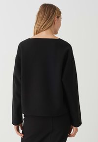 Zwarte cropped sweatshirt met een brede ronde hals, lange mouwen en een zachte textuur. Gladde stofafwerking met een relaxte pasvorm.