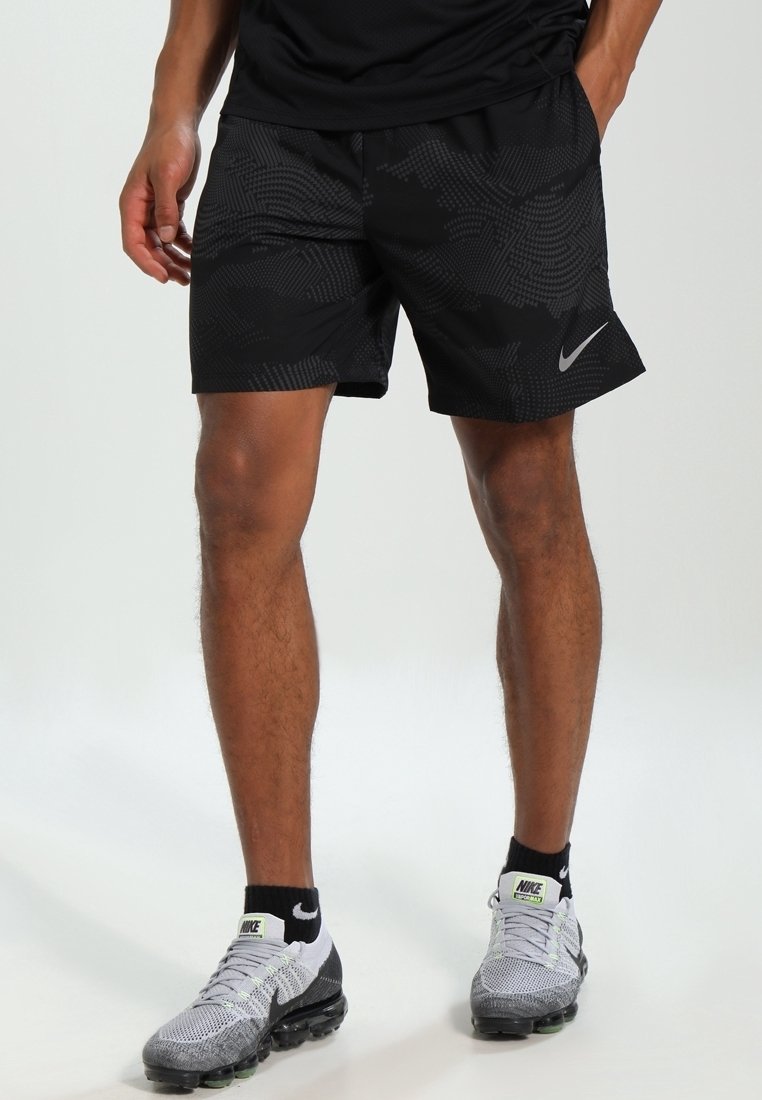 Svarta Nike-shorts med ett texturerat mönster, elastisk midja och en silverlogotyp. Bärs med grå träningsskor och svarta strumpor.