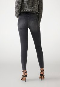 Zwarte skinny jeans met een gladde textuur, een middenhoog taille en twee achterzakken. Draagt het met zwarte spijkerhakken.