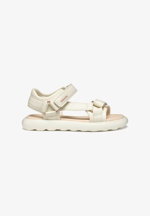 Sandalias de piel sintética blanca con correas de Velcro ajustables, plantilla acolchada en color beige y suela de goma texturizada con un patrón ondulado.