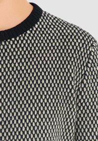 Maglione lavorato a maglia con motivo tridimensionale in blu navy e crema. Colletto nero a coste e tessuto morbido con un design aderente.