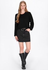 Zwarte gebreide trui, zwarte denimrok en kniehoge zwarte leren laarzen. De outfit heeft een riem met een zilveren gesp en textuurstoffen.