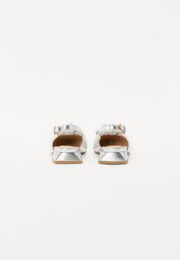 Silberne flache Sandalen mit einer glatten, metallischen Oberfläche, offenem Rücken und kleiner, dekorativer Schnalle. Sie verfügen über einen niedrigen Absatz und eine beigefarbene Innensohle.