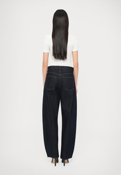 Široké tmavomodré džínsové nohavice s vysokým pásom, zadnými vreckami a jemnými švami, skombinované s priliehavou bielou košeľou.