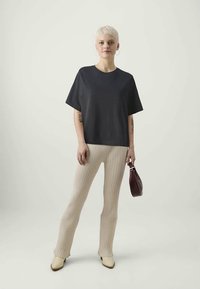 Fekete, oversize póló, bézs bordázott, bővülő nadrág és krém színű bokacsizma. A modell egy kicsi, bordó kézitáskát tart. Simaság és laza fazon.