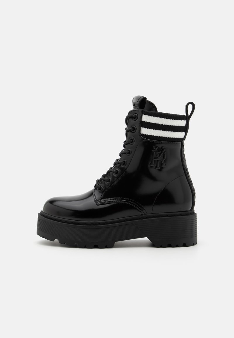 Black patent leather ankle boot with a chunky sole, featuring a lace-up front and striped knit collar. Logo detail on side.