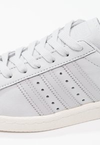 Gray leather sneaker with flat laces, textured side stripes, perforated detailing, and a rubber sole. Classic, low-profile design.