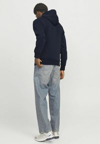 Felpa blu navy con cappuccio regolabile, polsini e orlo a coste. Abbinata a jeans larghi blu chiaro e scarpe da ginnastica argento.