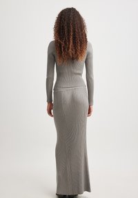Graues geripptes Strickkleid mit einer enganliegenden Silhouette, langen Ärmeln und einem langen Rock. Die glatte Textur und die vertikalen Linien erzeugen eine einheitliche Optik.