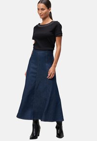 Zwarte top met korte mouwen en decoratieve studs bij de halslijn, gecombineerd met een lange donkerdenimrok en zwarte enkellaarsjes met hak.
